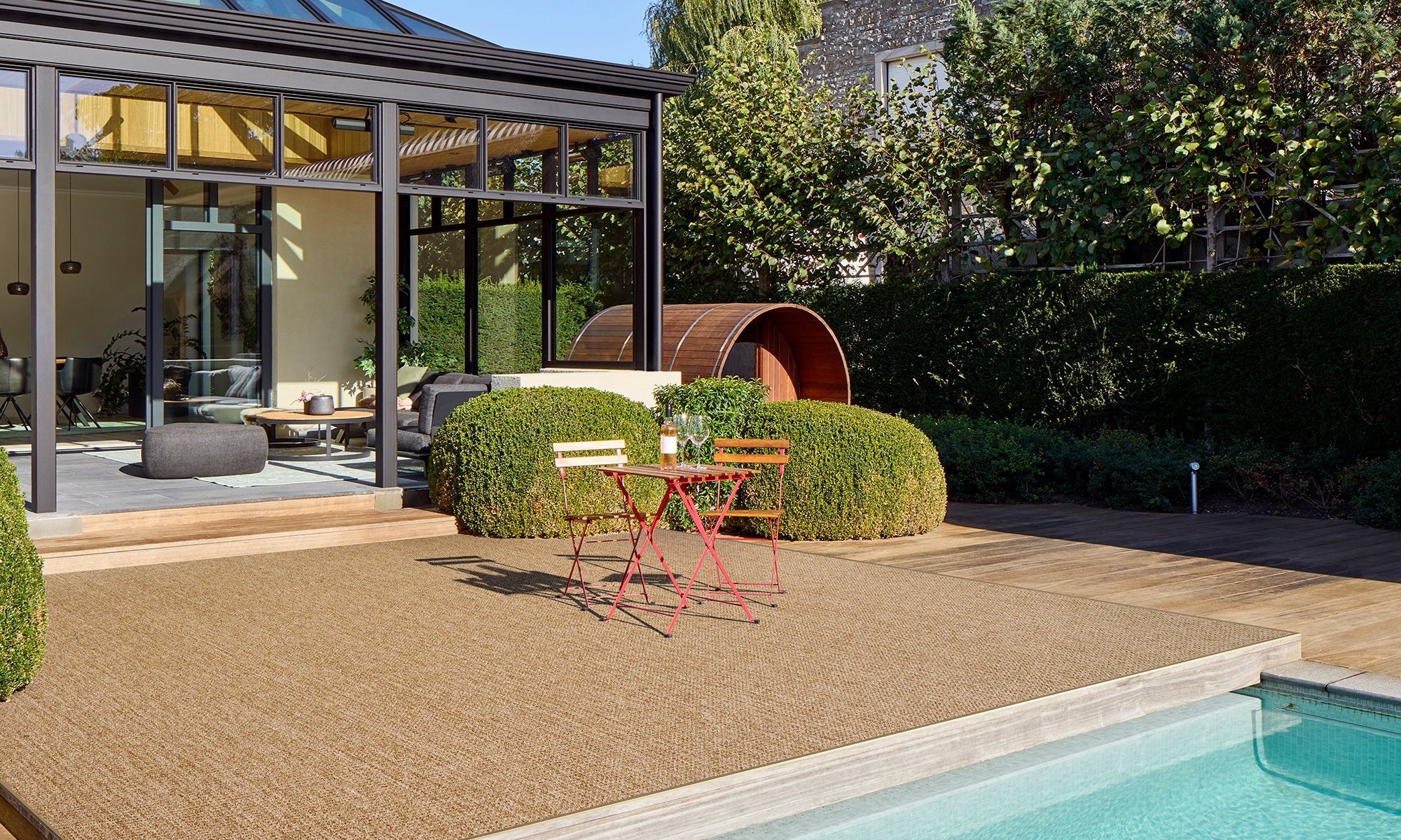 Modern outdoor patio with pool, deck chairs, and a glass-enclosed room.