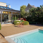 Modern outdoor patio with pool, deck chairs, and a glass-enclosed room.