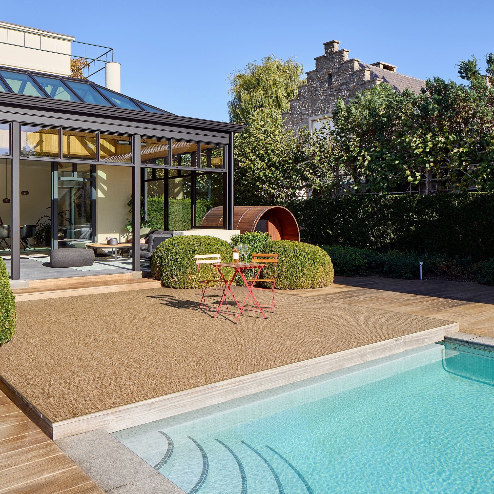 Modern outdoor patio with pool, deck chairs, and a glass-enclosed room.